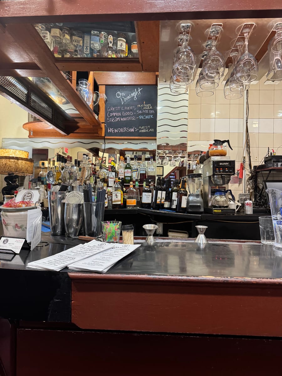 The Free Times bar: hanging glasses, bottles on the back shelf and the chalkboard of draught beers