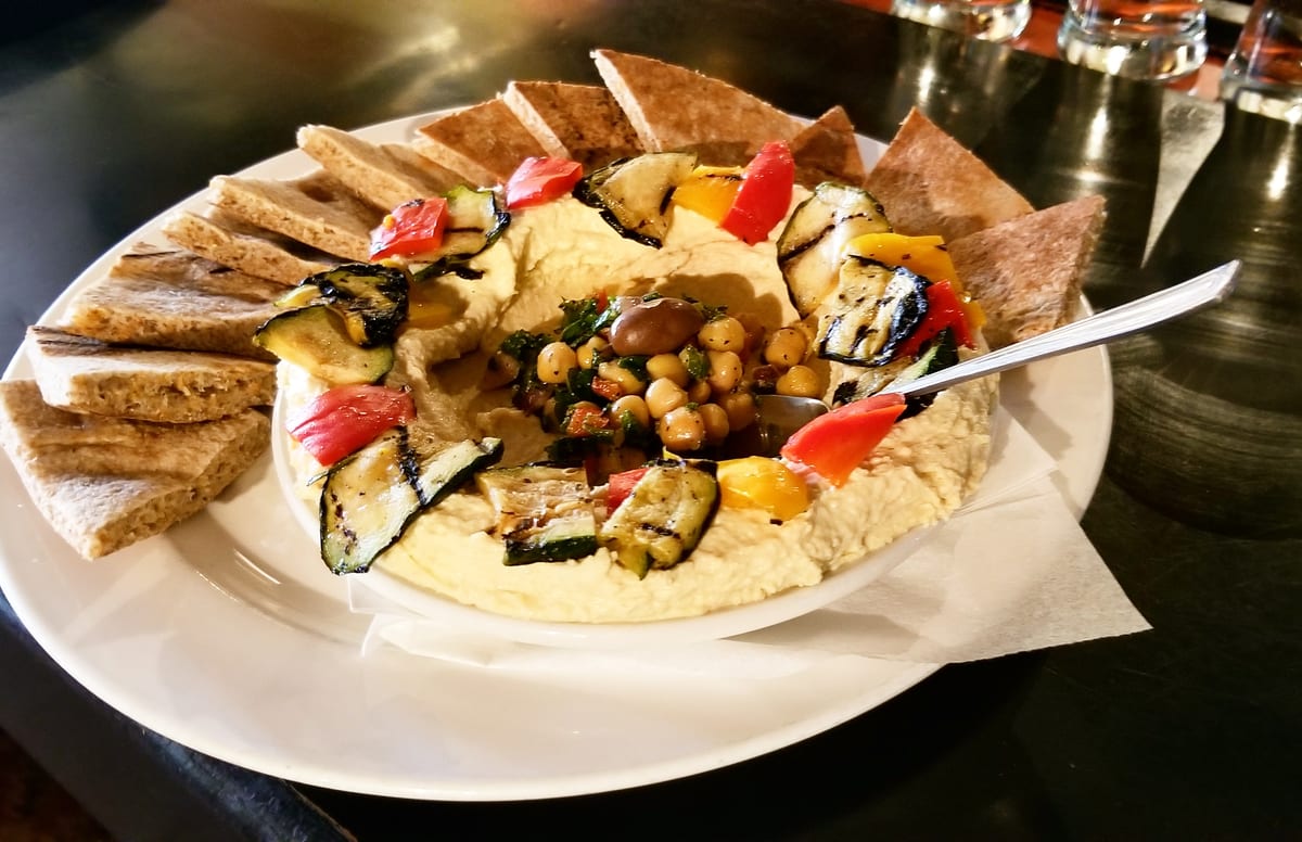 A plate of hummus topped with grilled eggplant, peppers and chickpeas, with toasted pita, on a table at Free Times Cafe