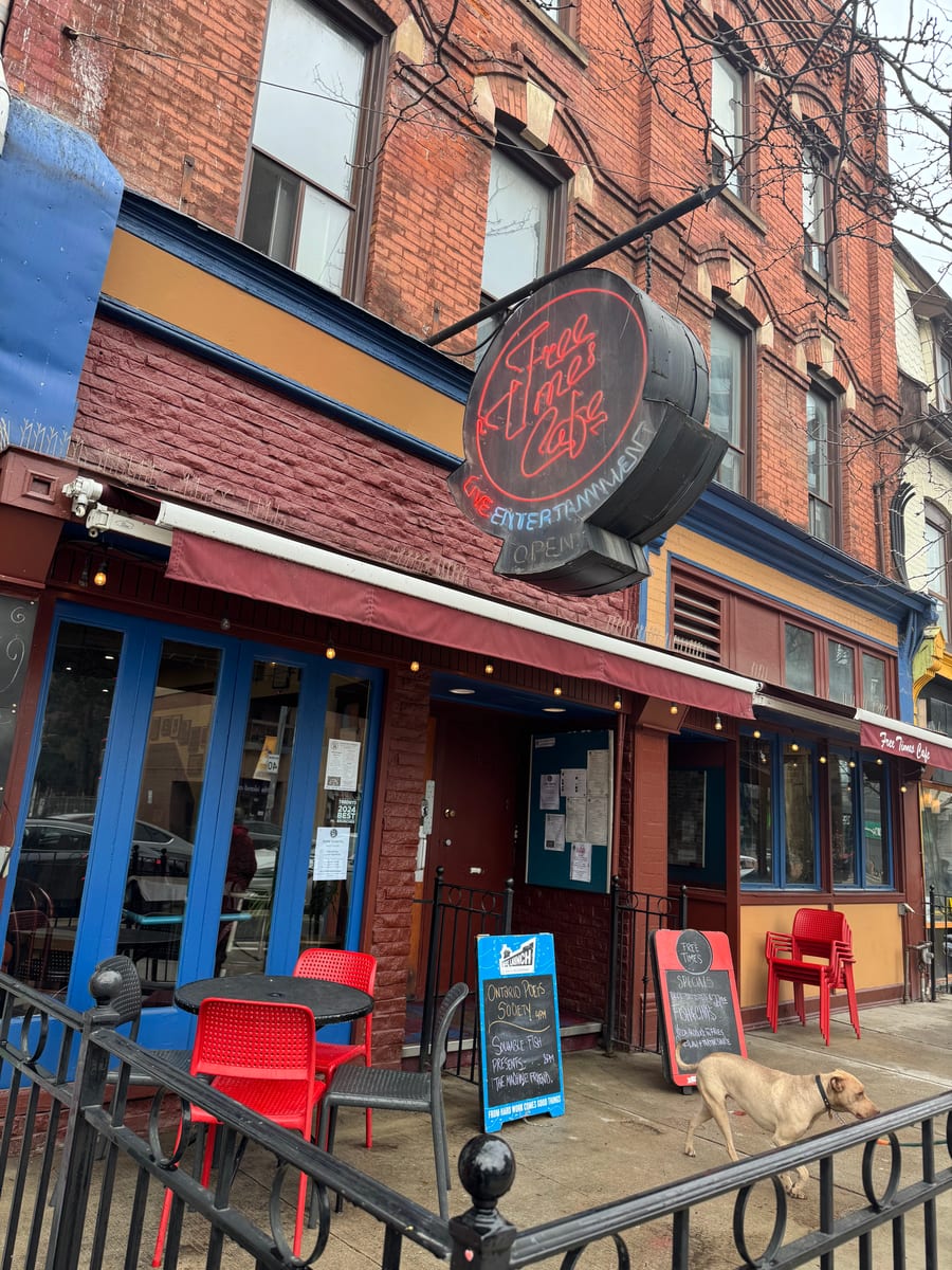 The Free Times Cafe storefront on College Street: red brick, blue-trimmed doors, the round neon sign and red patio chairs