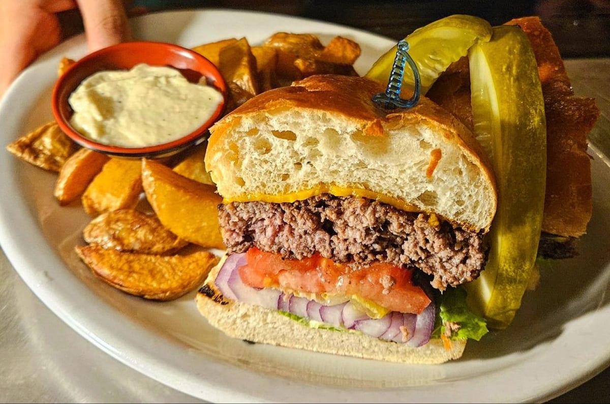 A cheeseburger with tomato and red onion, potato wedges, a pickle and garlic mayo